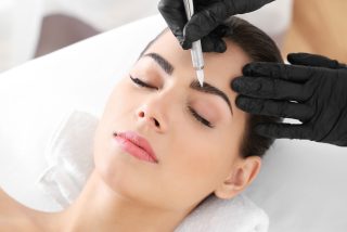 Young woman undergoing procedure of eyebrow permanent makeup in beauty salon